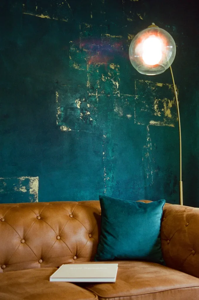 A brass arc lamp lit above a tan chesterfield against emerald and gold plaster in the open-plan living space