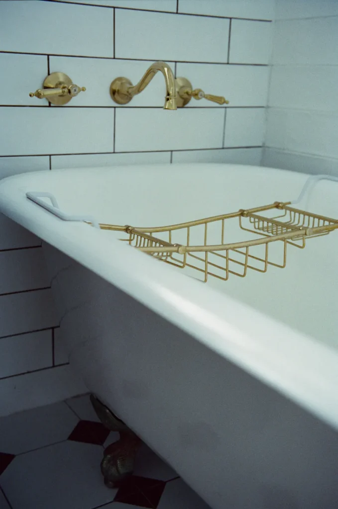 A clawfoot bath with a brass rack and brass tapware, checkerboard tile underfoot