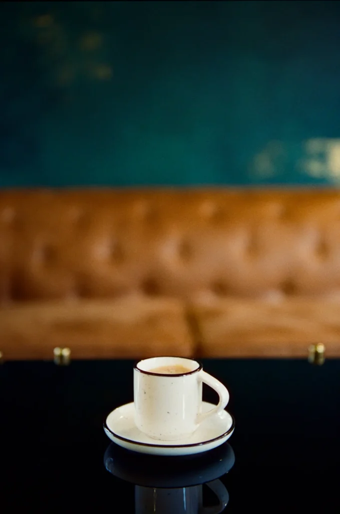 An espresso cup on a dark table with tufted leather behind
