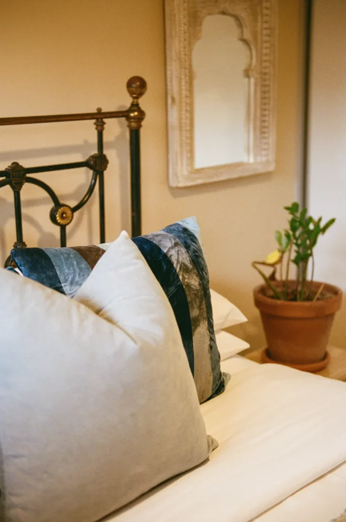 A brass bed with blue and olive velvet cushions, a carved mirror behind.