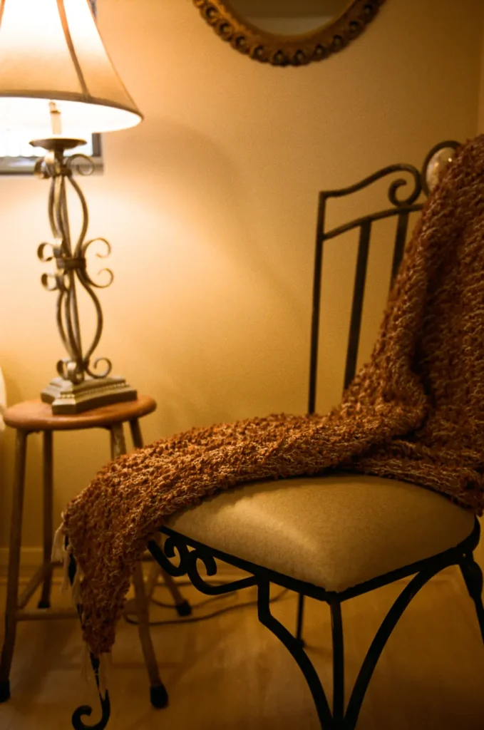 A wrought iron chair with a bouclé throw draped over it beside a lamp