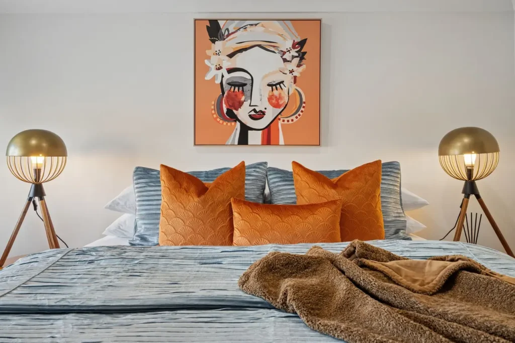 The Amber bed at The Mooring, orange cushions and twin globe lamps beneath a portrait