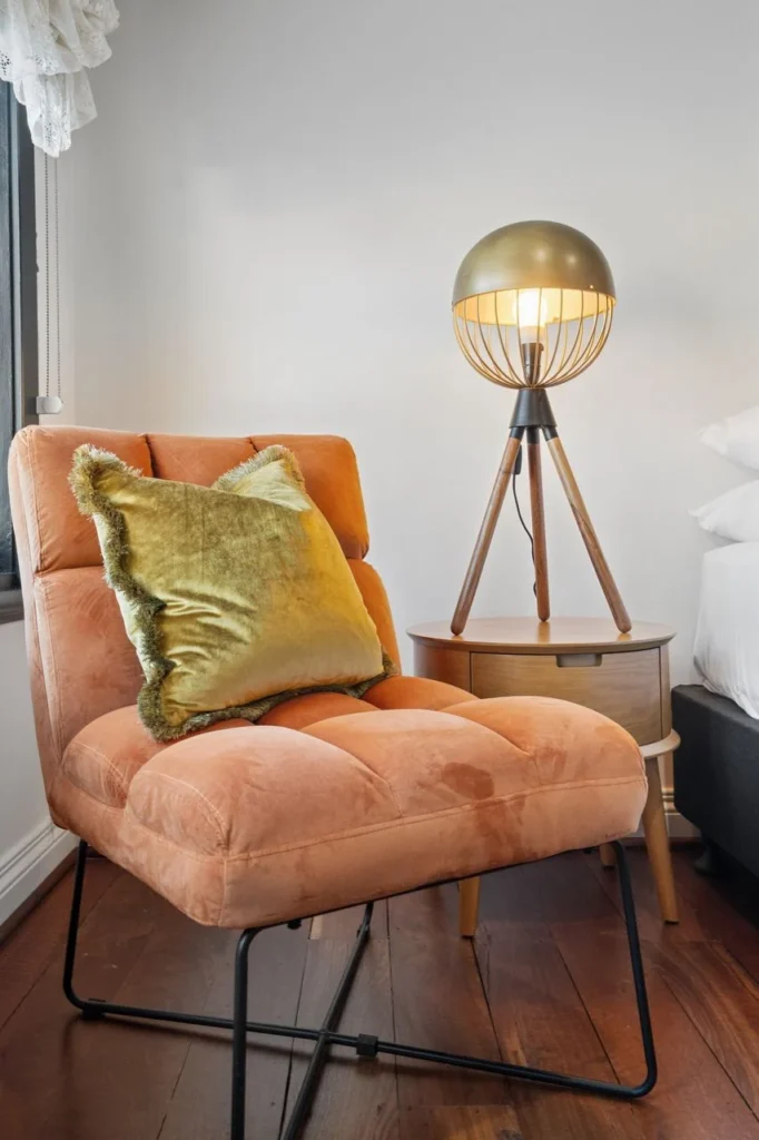 An orange velvet armchair beside a globe lamp on a timber tripod