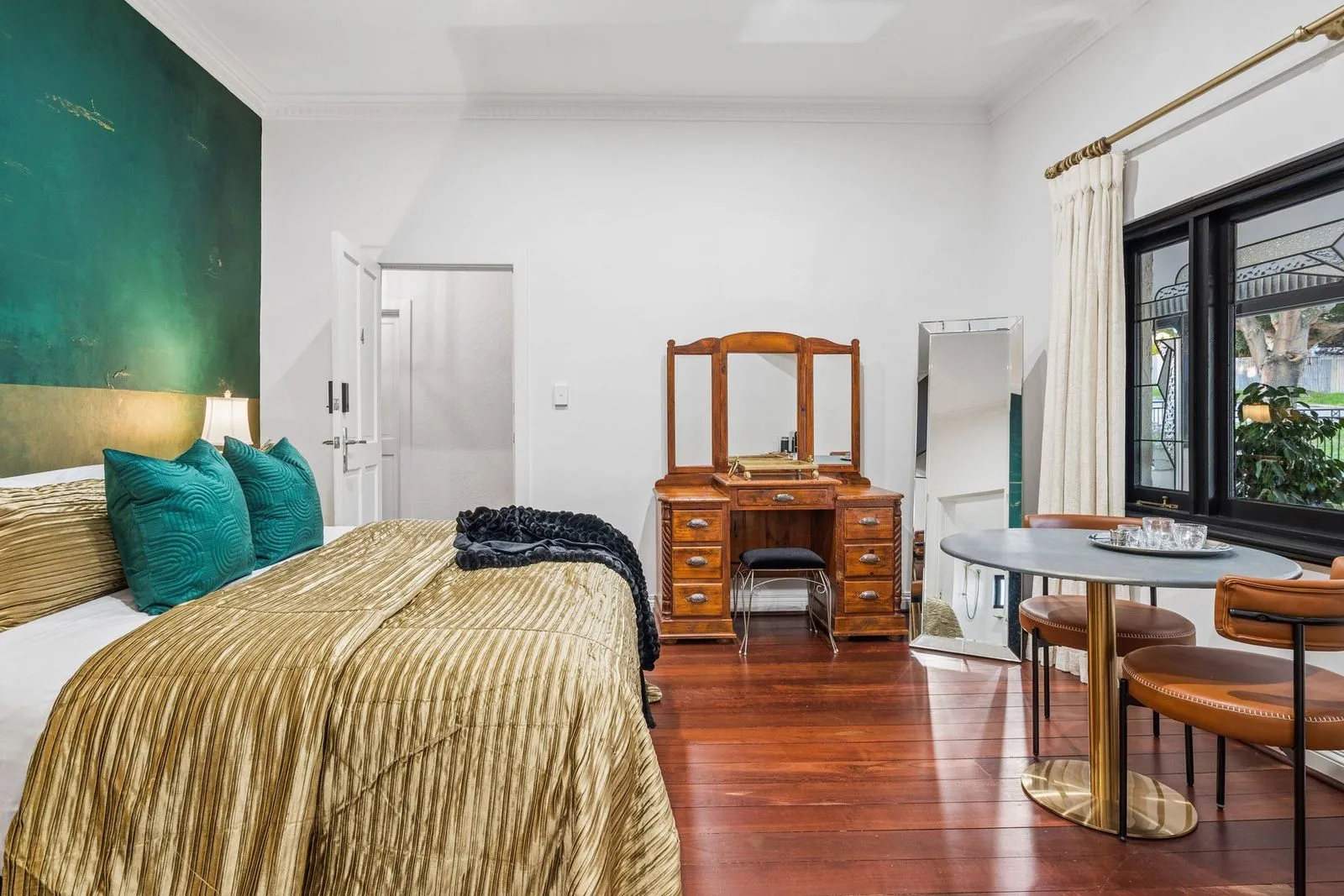 The Emerald room at The Mooring, green over gold wall, carved timber dresser and a bistro table by the window