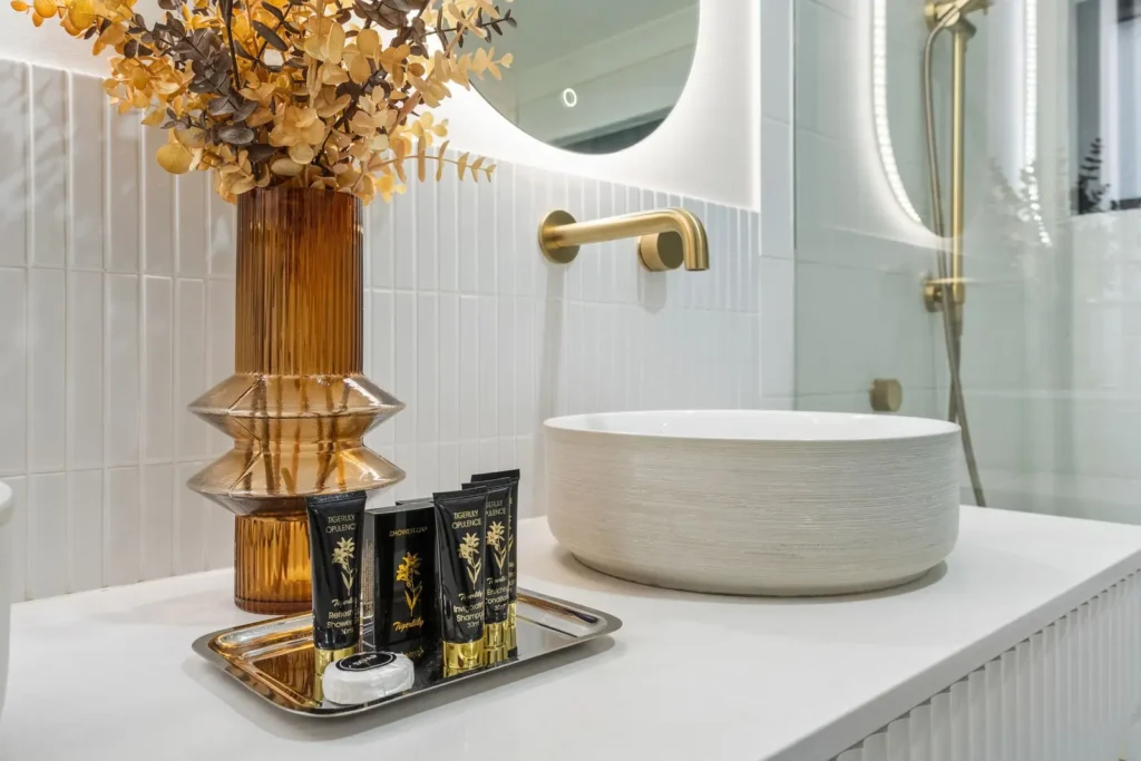 An amber fluted vase and toiletries on a brass tray beside a stone basin