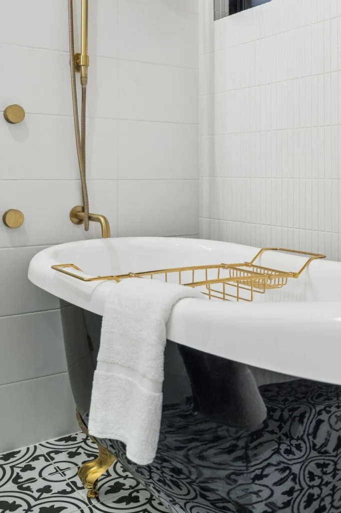A clawfoot bath with a brass rack across it, patterned tile underfoot