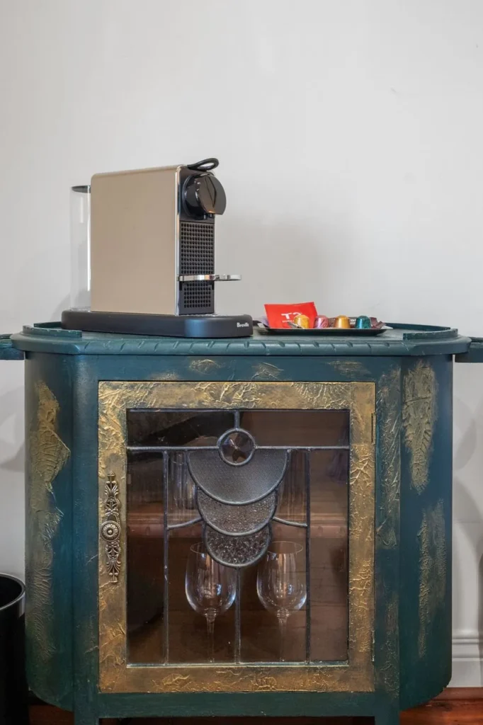 A green and gold cabinet with a leadlight door and a coffee machine on top