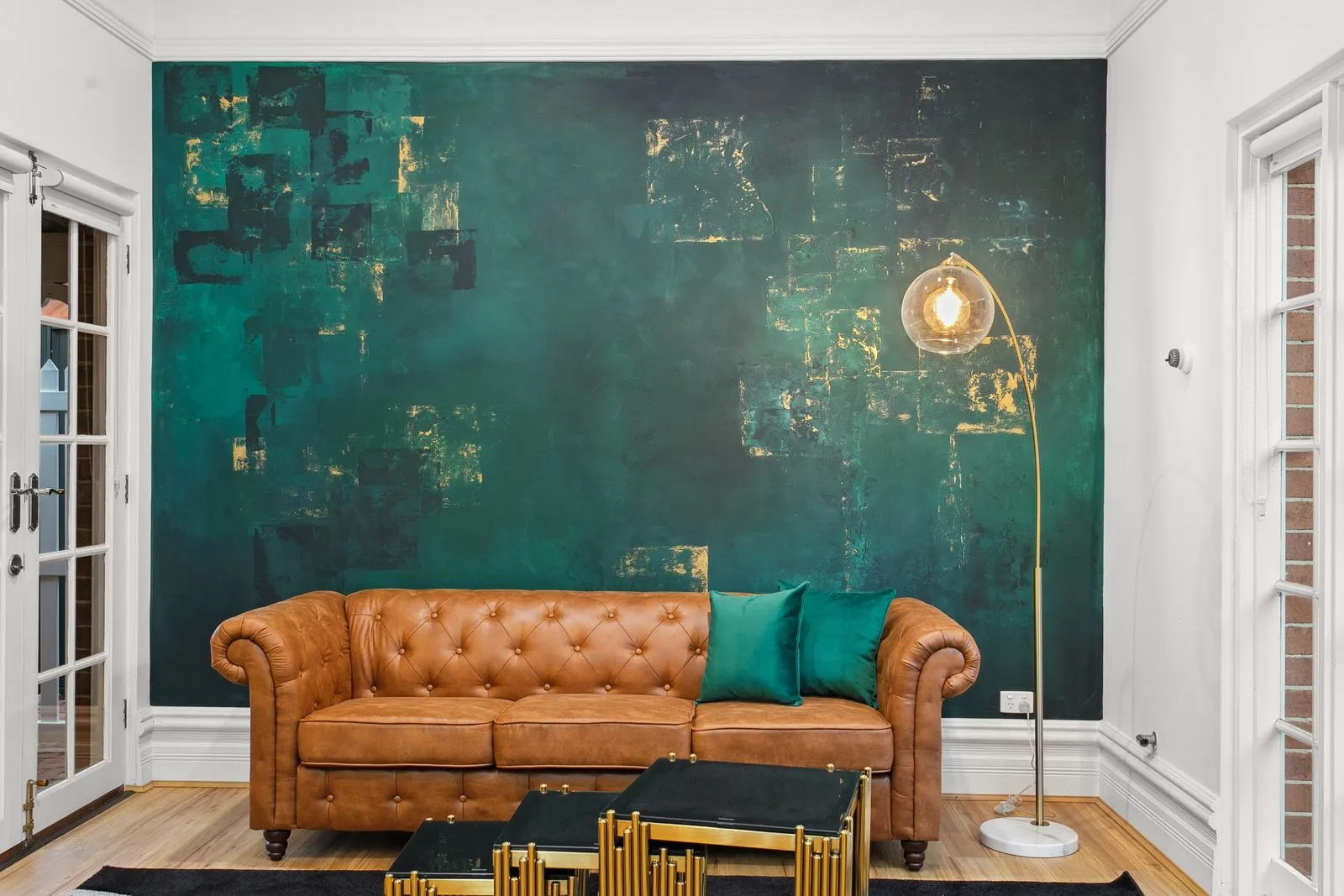 Tan leather chesterfield against the emerald and gold feature wall in the open-plan kitchen and dining at The Sapphire House