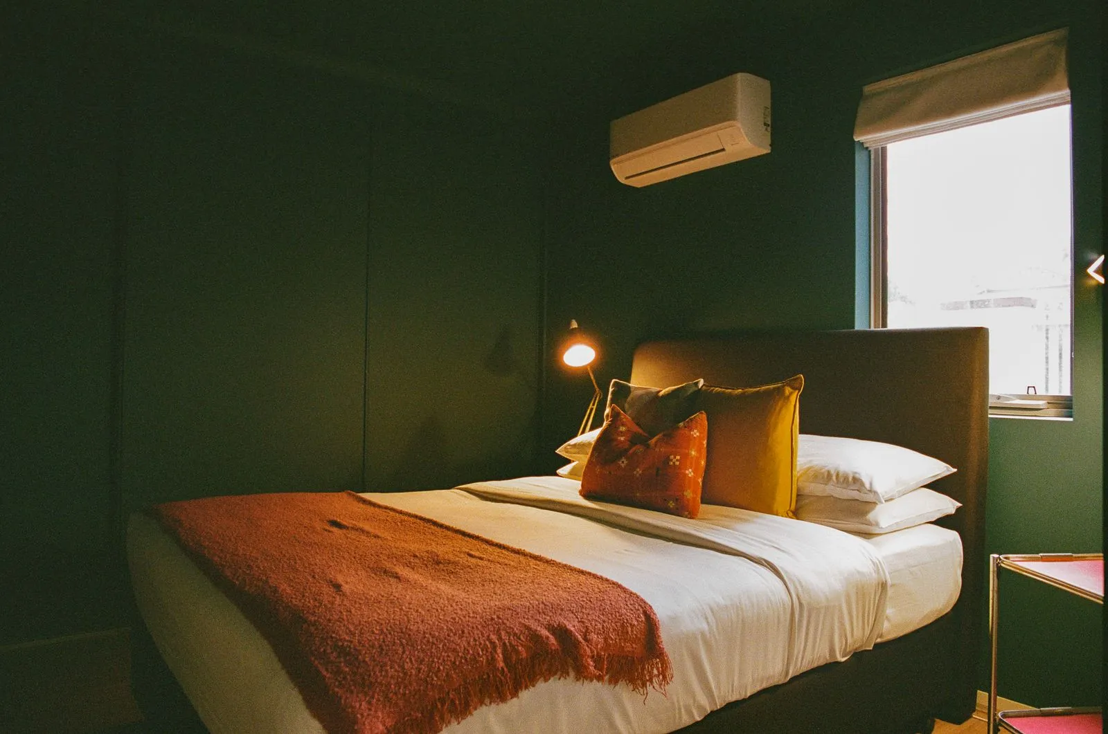 A bed made up in white with a rust throw, against dark green walls