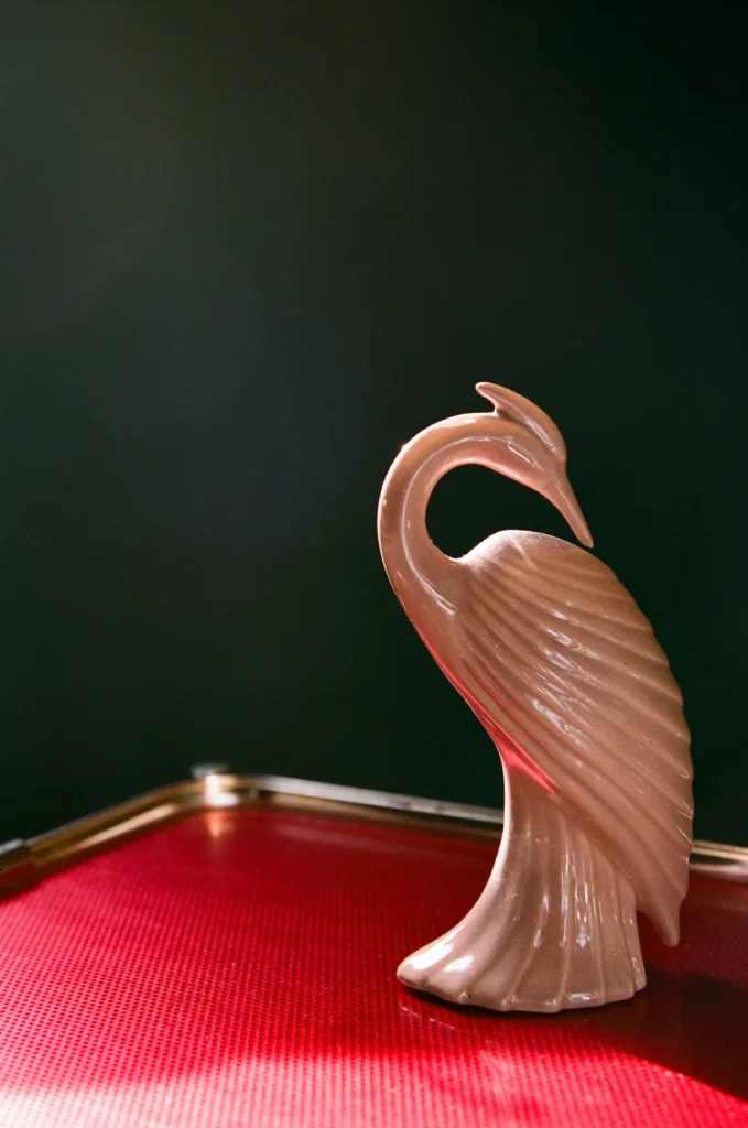 A pink ceramic crane standing on a red lacquer tray