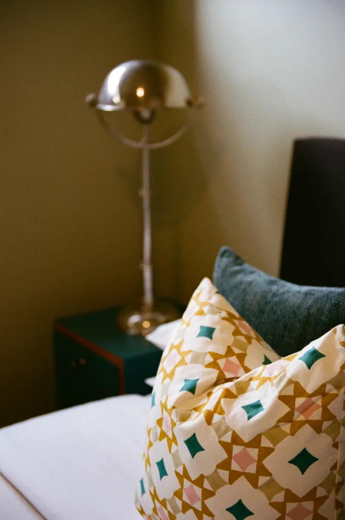 A chrome lamp beside a bed with a patterned cushion below