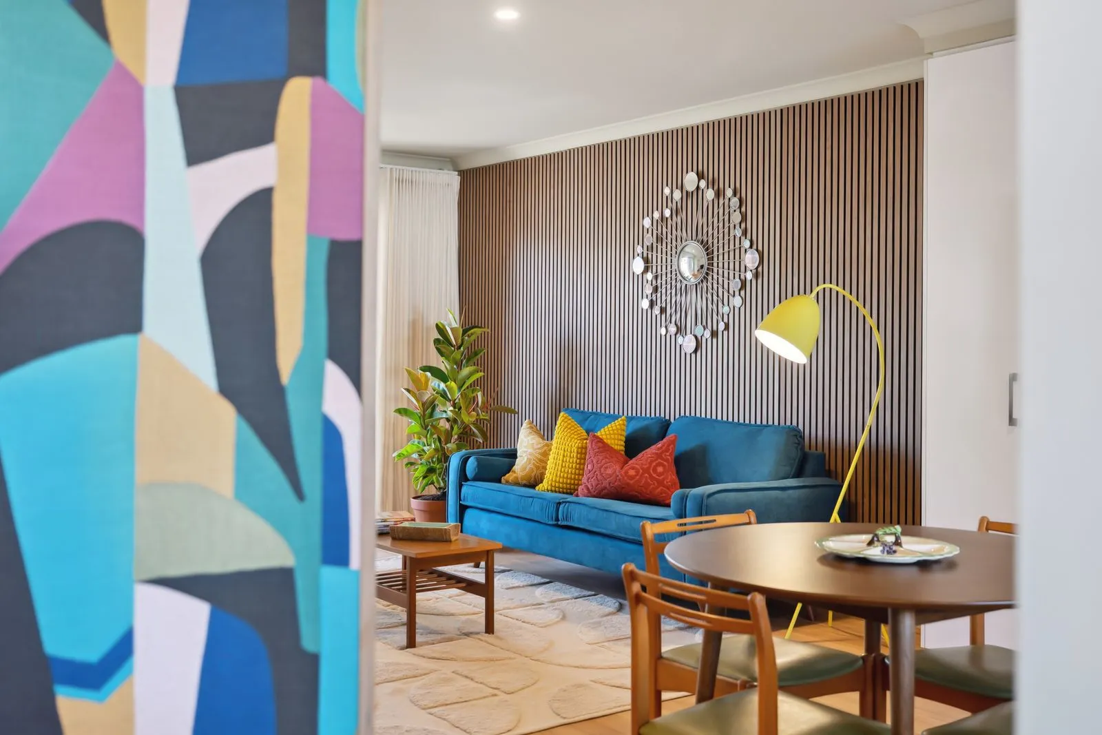 The living room at The Tonic seen past a panel of geometric wallpaper , blue sofa and timber batterns