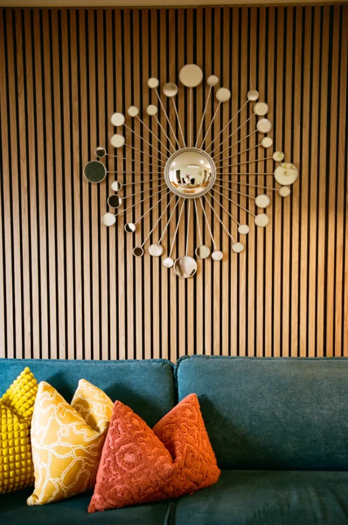 A starburst mirror on a timber batten wall above a teal sofa